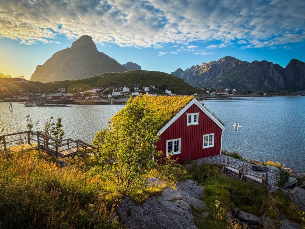 Red rorbu cabin on the shore at Reine, Lofoten, with mountains across the fjord, seen on our shore excursion from Leknes and Gravdal cruise port